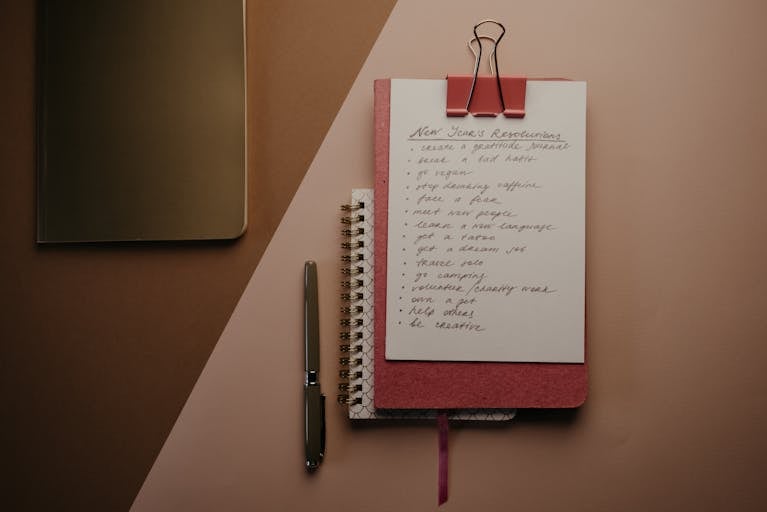 Top view of a cozy pink notebook with New Year resolutions, pen, and stylish paperclip setup.