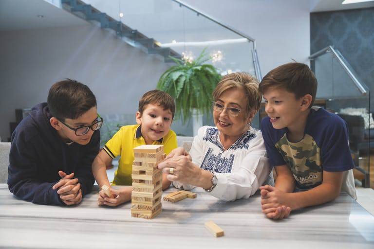 A joyful family moment with grandma and grandsons playing Jenga indoors, capturing quality time together.