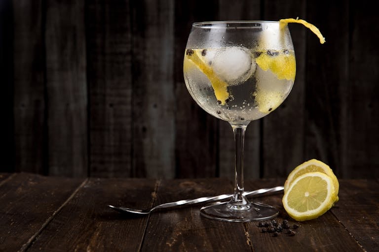 A close-up of a refreshing gin cocktail with lemon slices on a rustic wooden table, perfect for summer.
