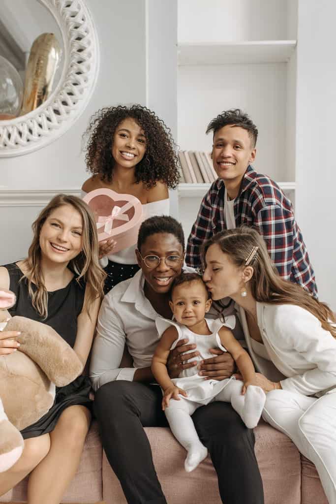 Group of diverse friends and family celebrating with smiles and gifts inside a cozy home.