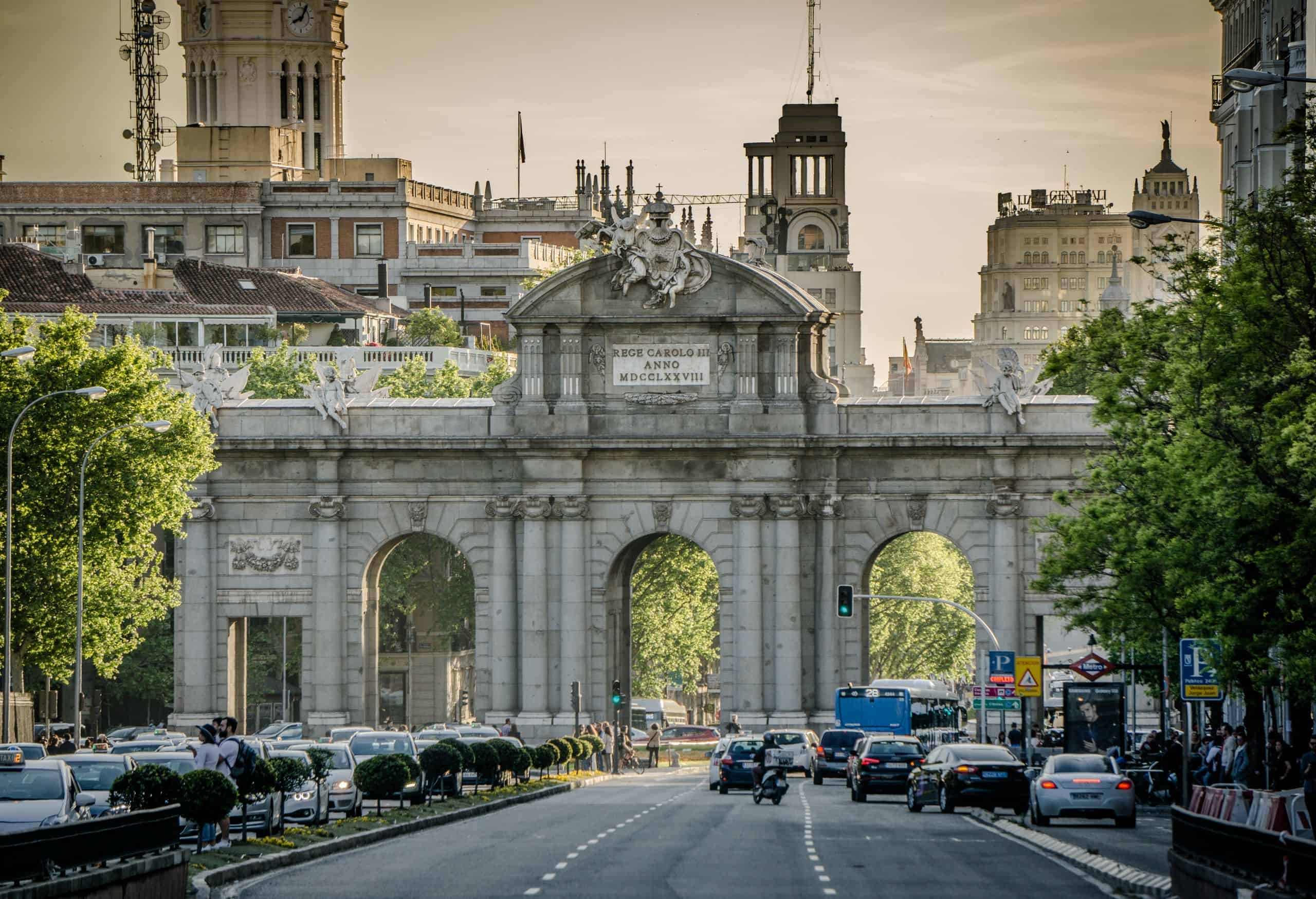 View of the historic Puerta de Alcalá in Madrid with traffic and city architecture.